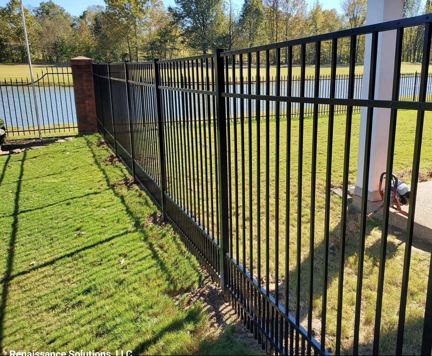 A black metal fence surrounds a lush green field.