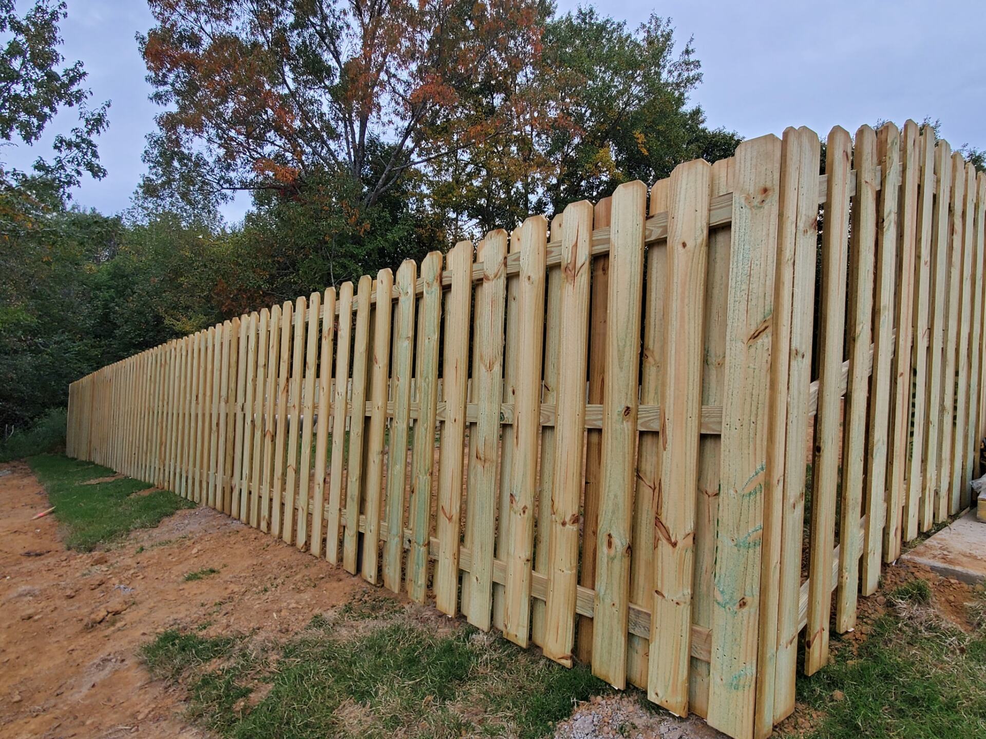 A long wooden fence is sitting next to a dirt road.