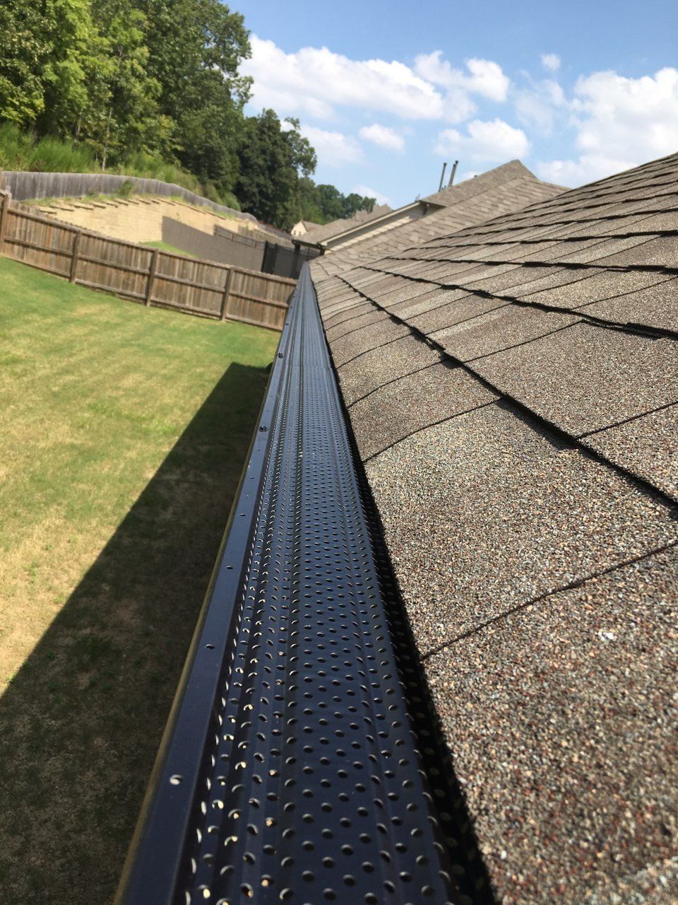 A gutter on the side of a roof with a fence in the background.