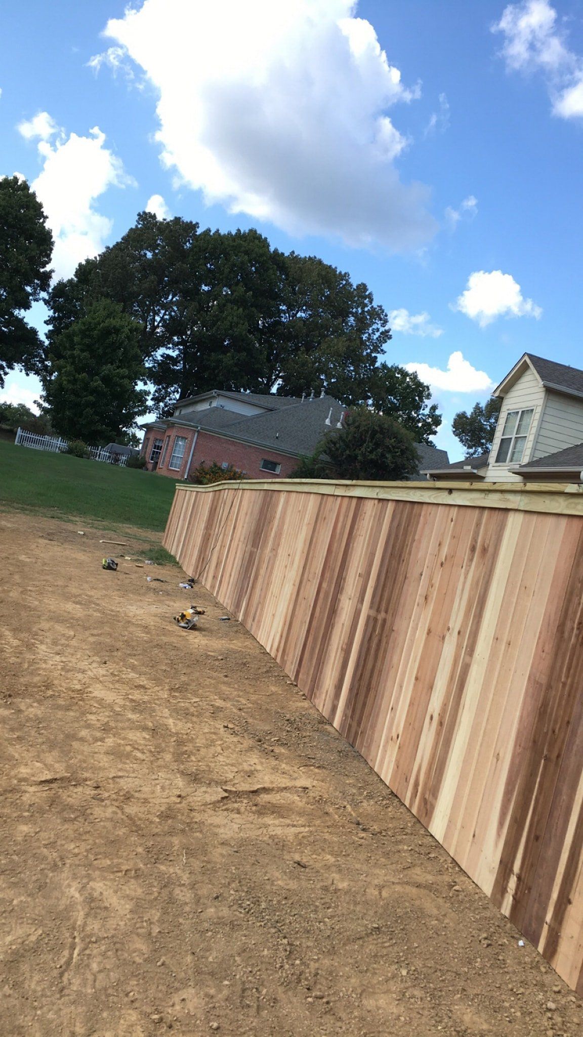 A large wooden fence is sitting on top of a dirt field next to a house.