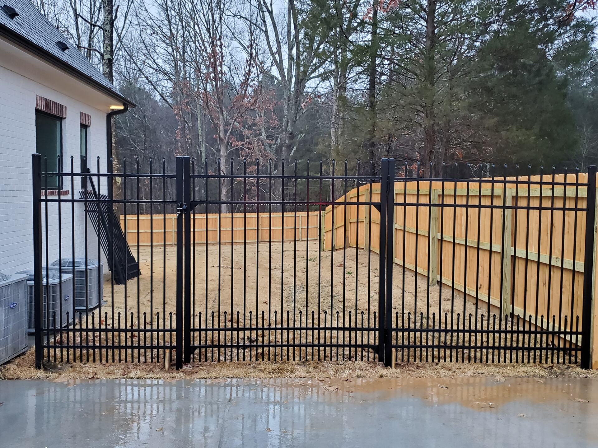 A black metal fence with a wooden fence behind it