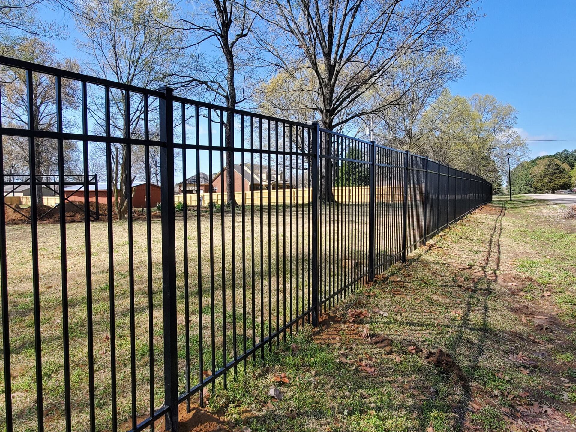 A black metal fence surrounds a grassy field with trees in the background.