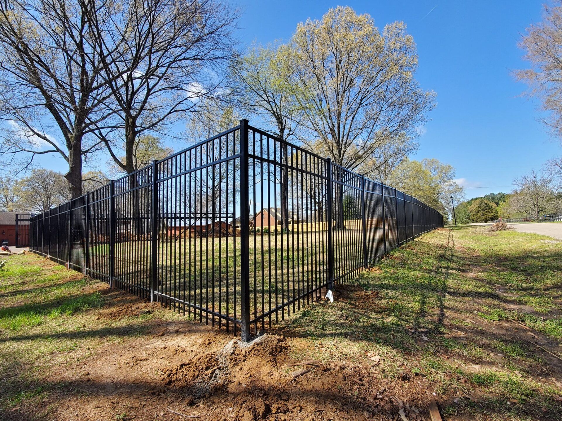 A black metal fence surrounds a grassy field with trees in the background.
