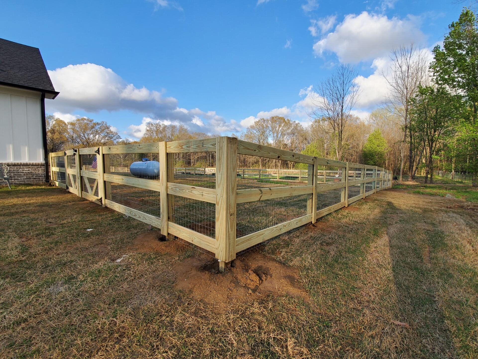 A wooden fence is surrounding a yard with a house in the background.