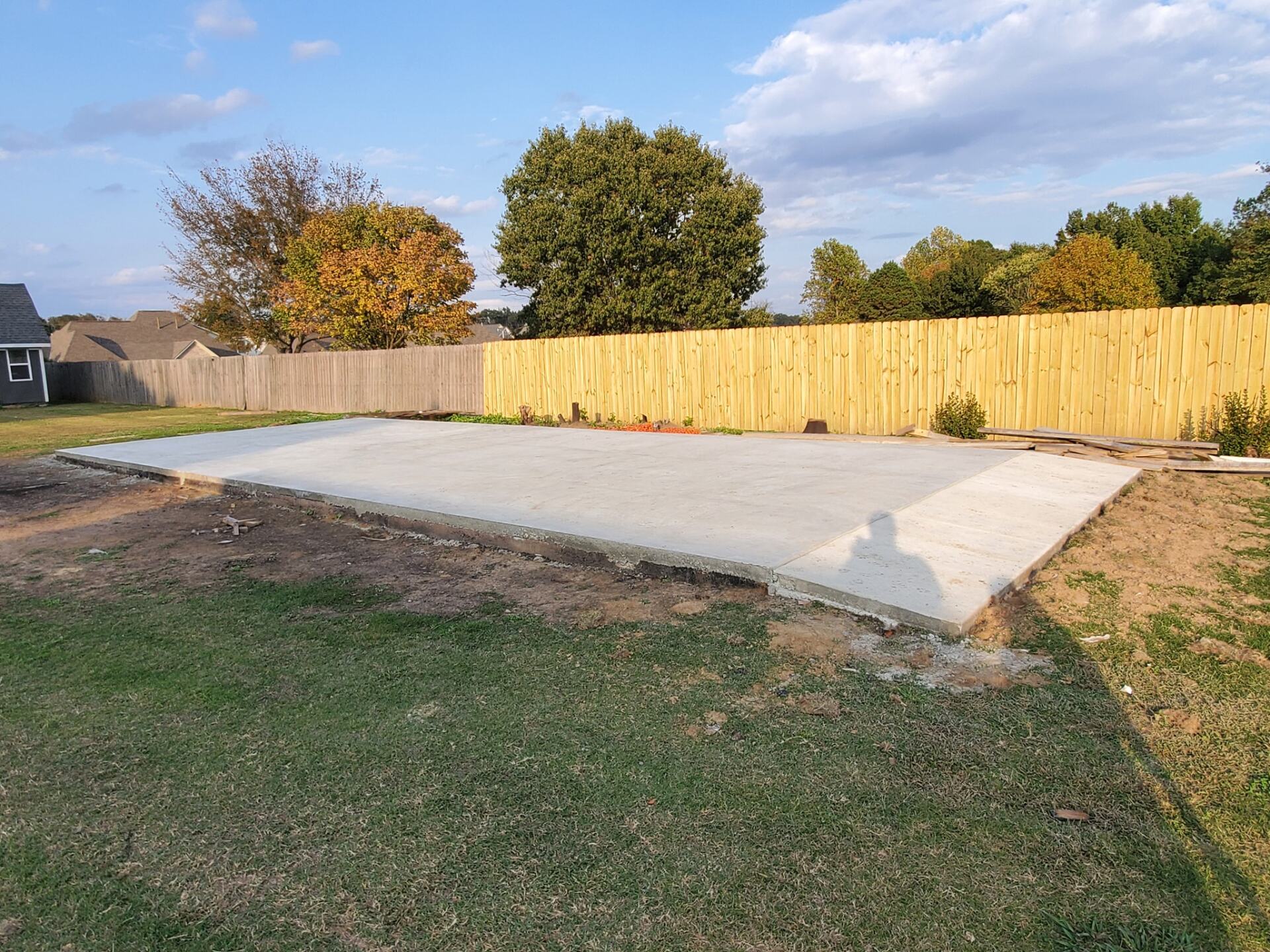 A large concrete slab in a backyard with a wooden fence in the background.