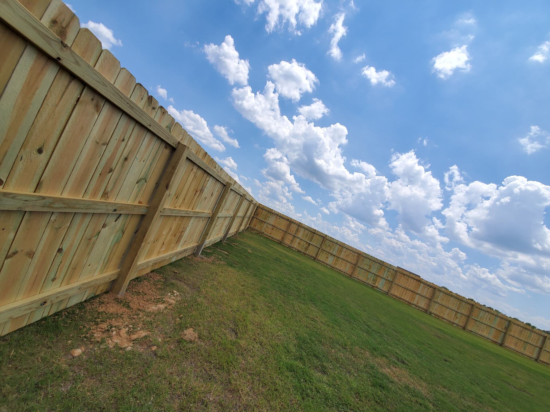 A wooden fence surrounds a grassy field with a blue sky in the background