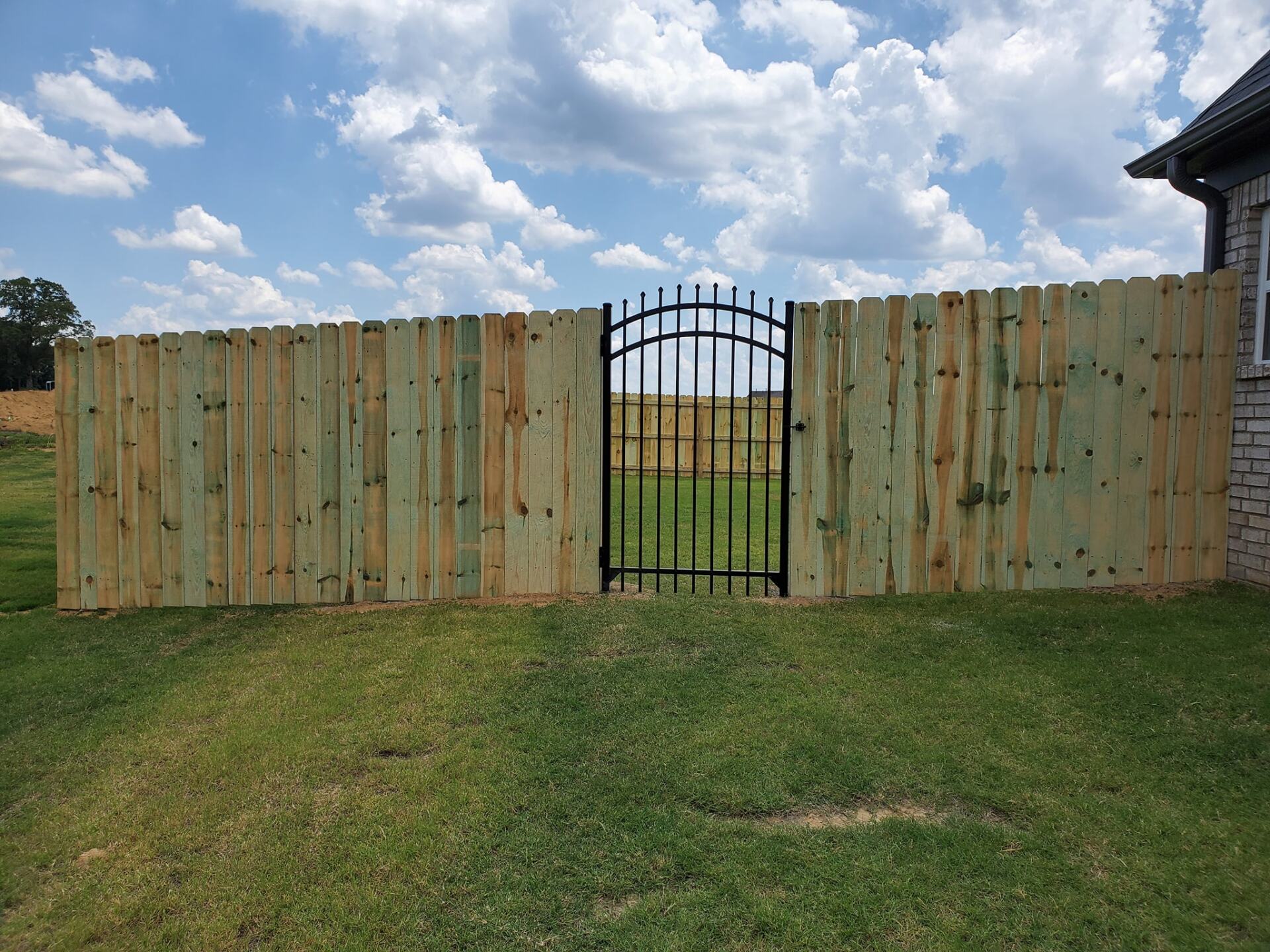 A wooden fence with a metal gate in the middle of it.