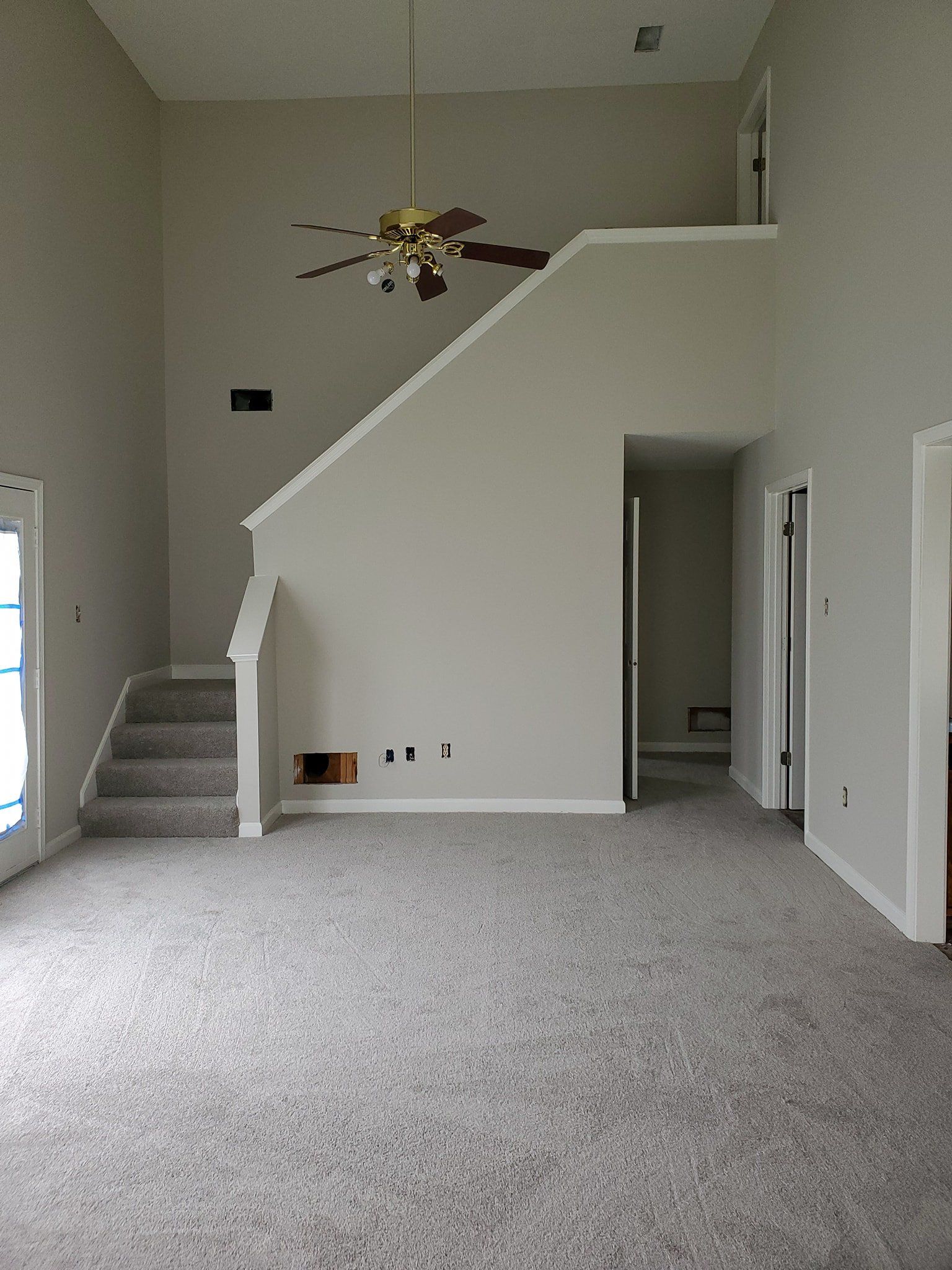 An empty living room with stairs and a ceiling fan.