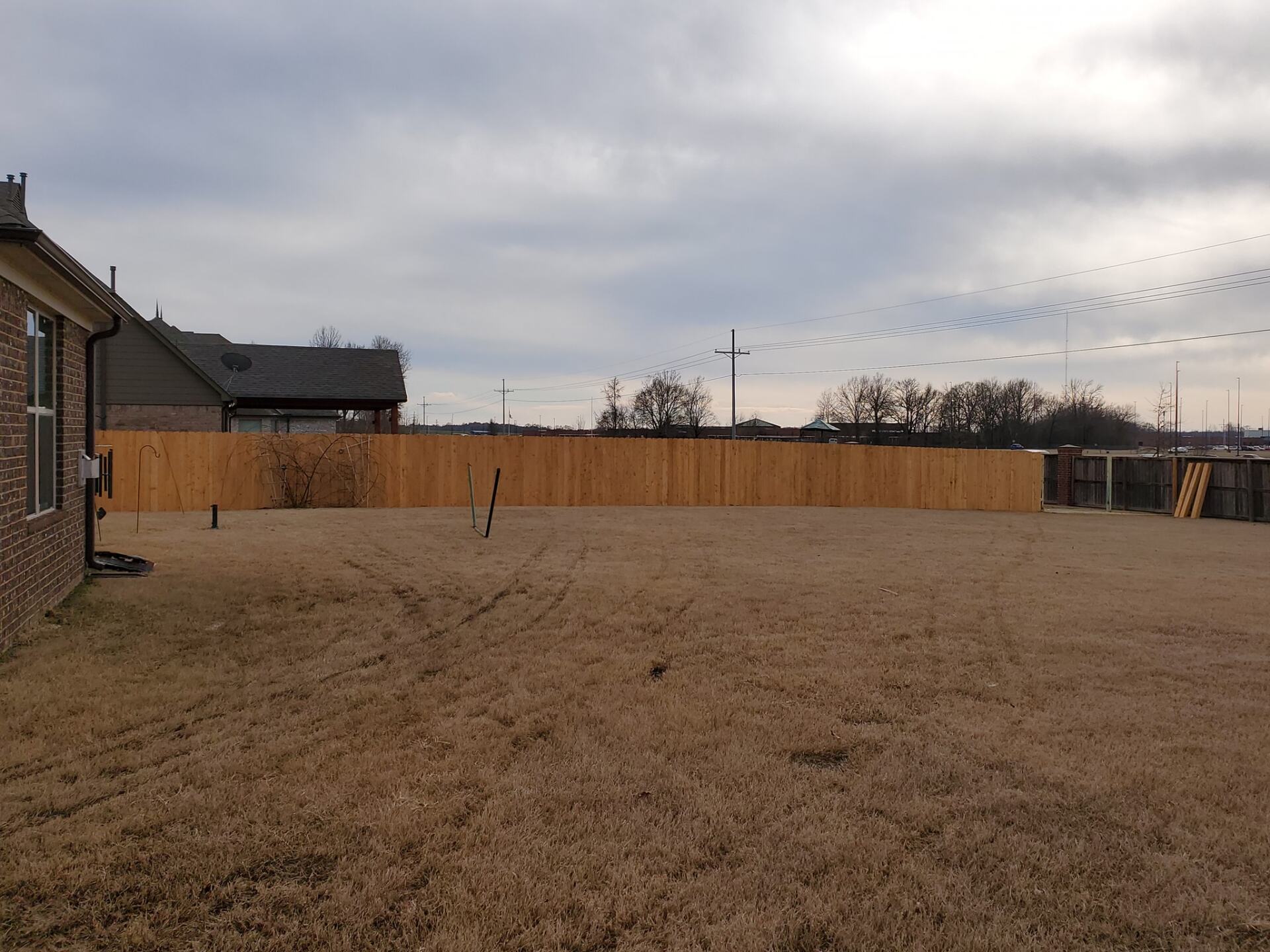 A backyard with a wooden fence and a house in the background