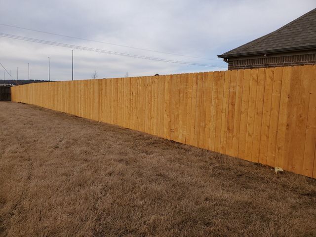 A long wooden fence surrounds a dirt field in front of a house.