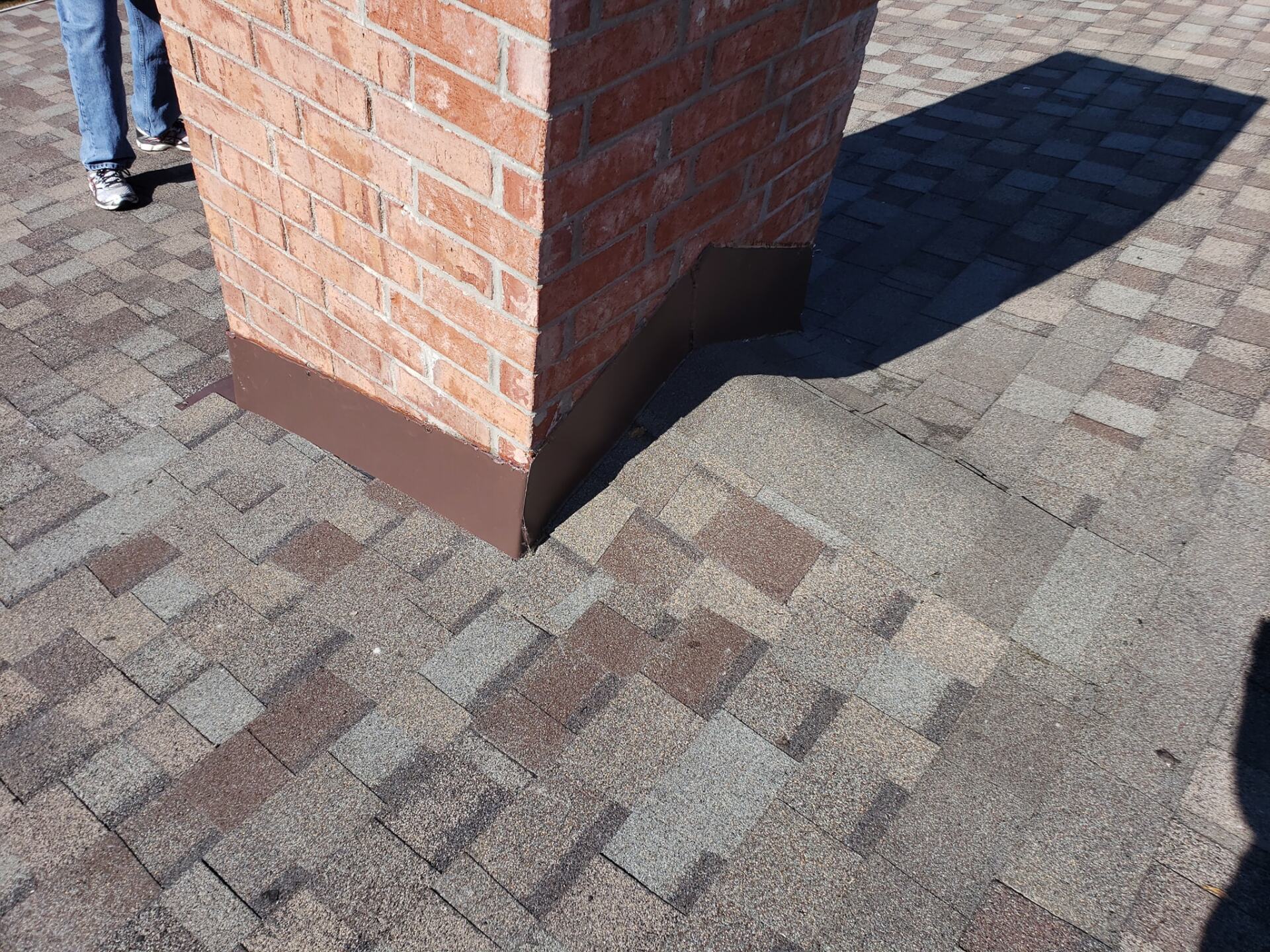 A person is standing next to a brick chimney on a brick sidewalk.