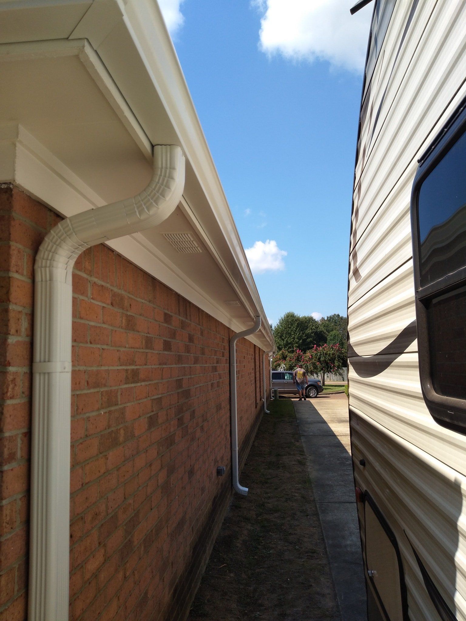 A brick house with a white gutter next to a trailer.