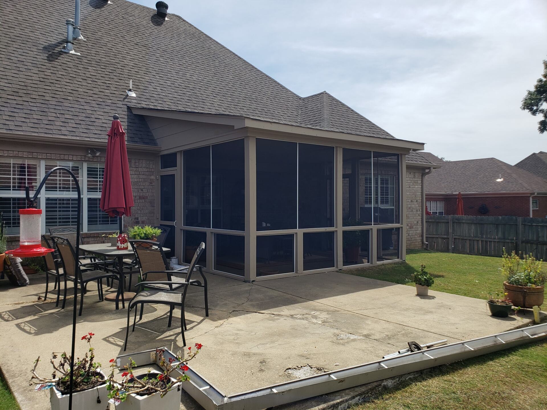 A screened in porch with a table and chairs in the backyard of a house.