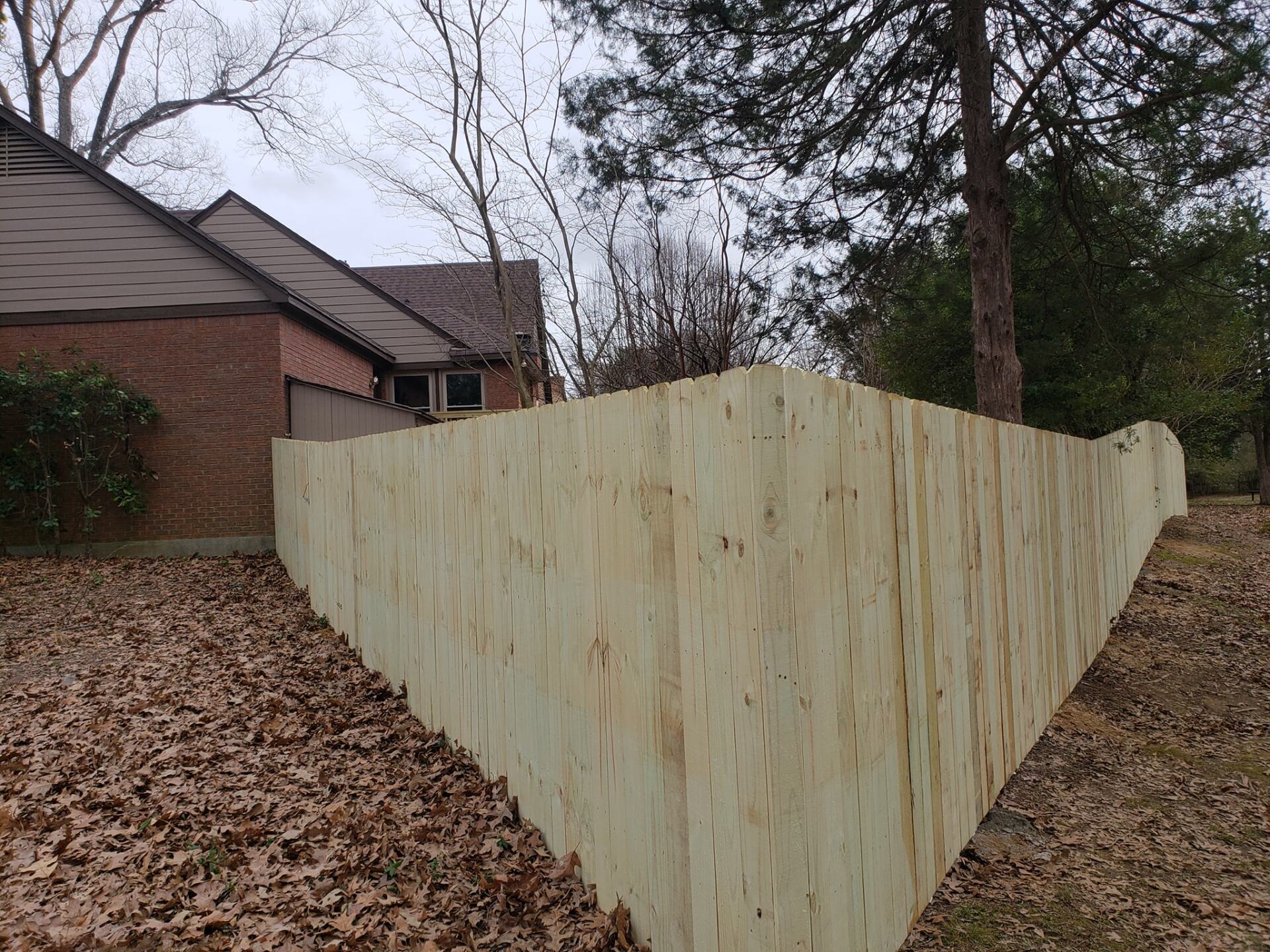 A wooden fence is surrounded by trees and leaves in front of a house.
