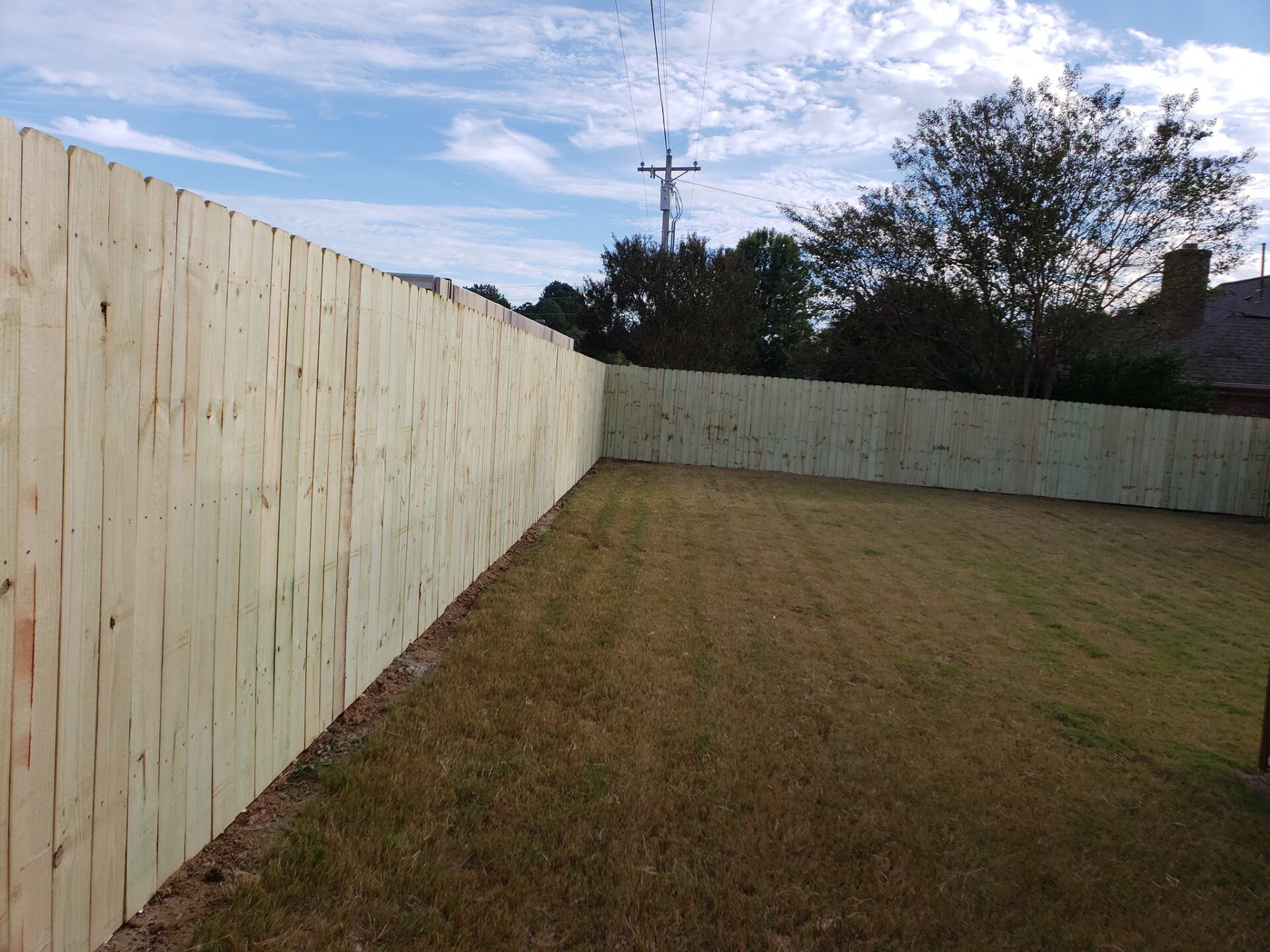 A wooden fence surrounds a lush green yard.