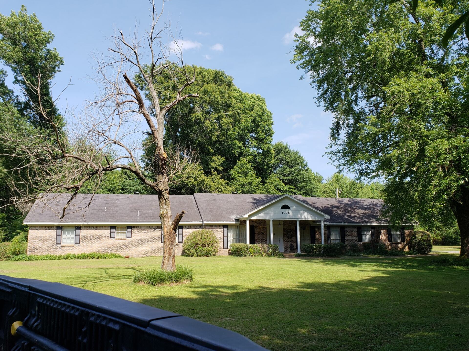 A brick house with a porch and trees in front of it
