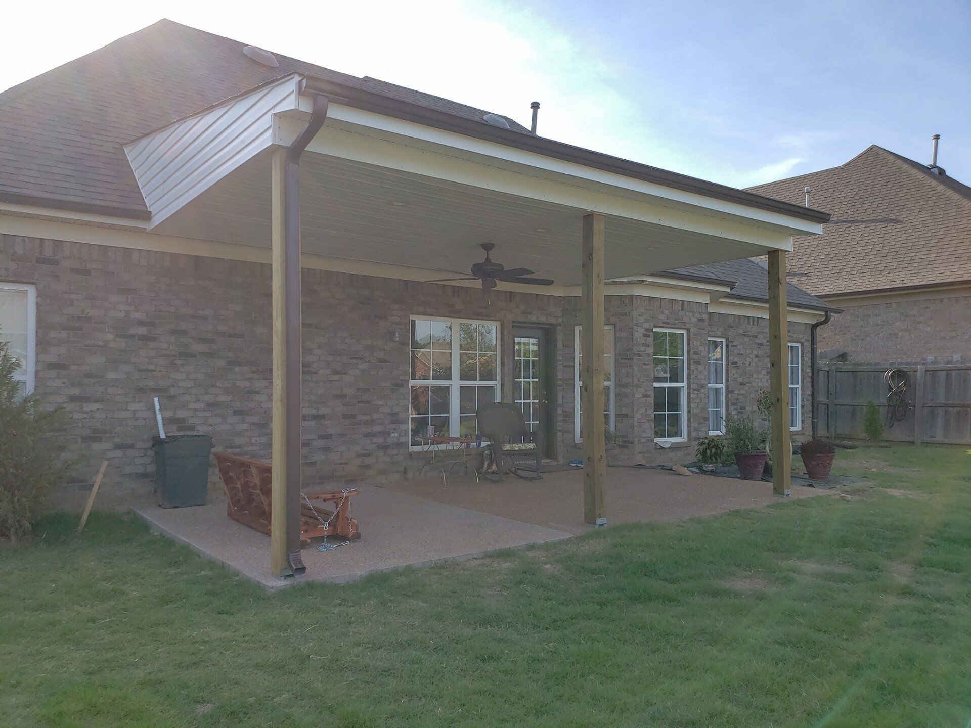 There is a patio with a ceiling fan in the backyard of a house.