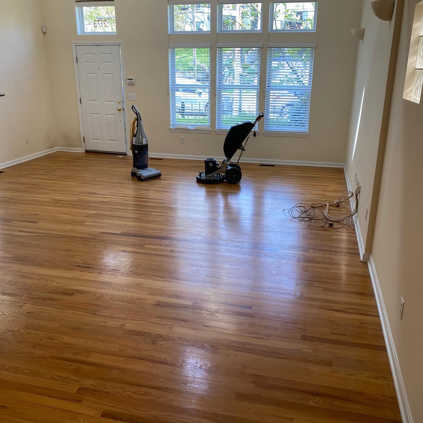 Hardwood floors in a brightly lit room with a vacuum and a floor buffer machine in the center.