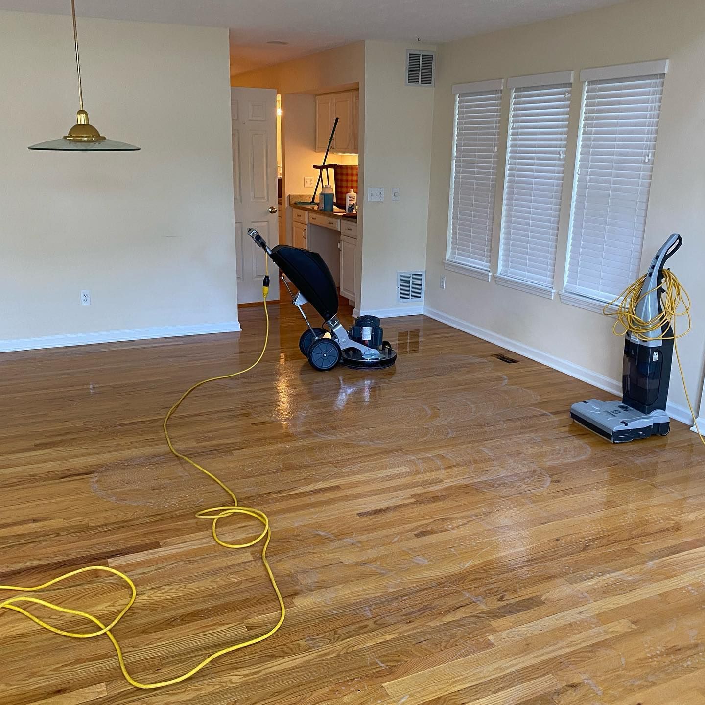 Hardwood floors in a home being cleaned with a large circular floor buffer and a standing vacuum.