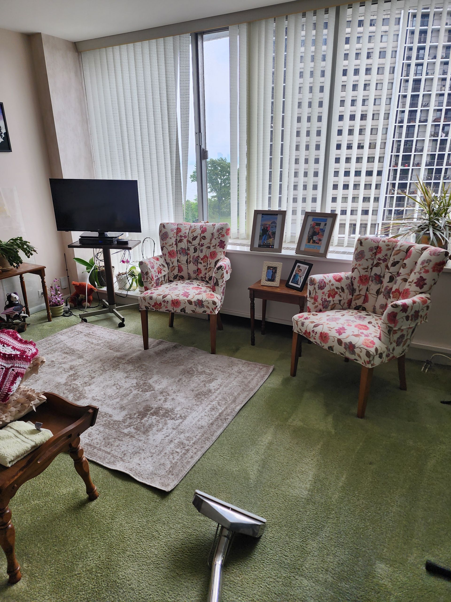 Bright living room with floral chairs, small TV, side table, and city view through tall windows