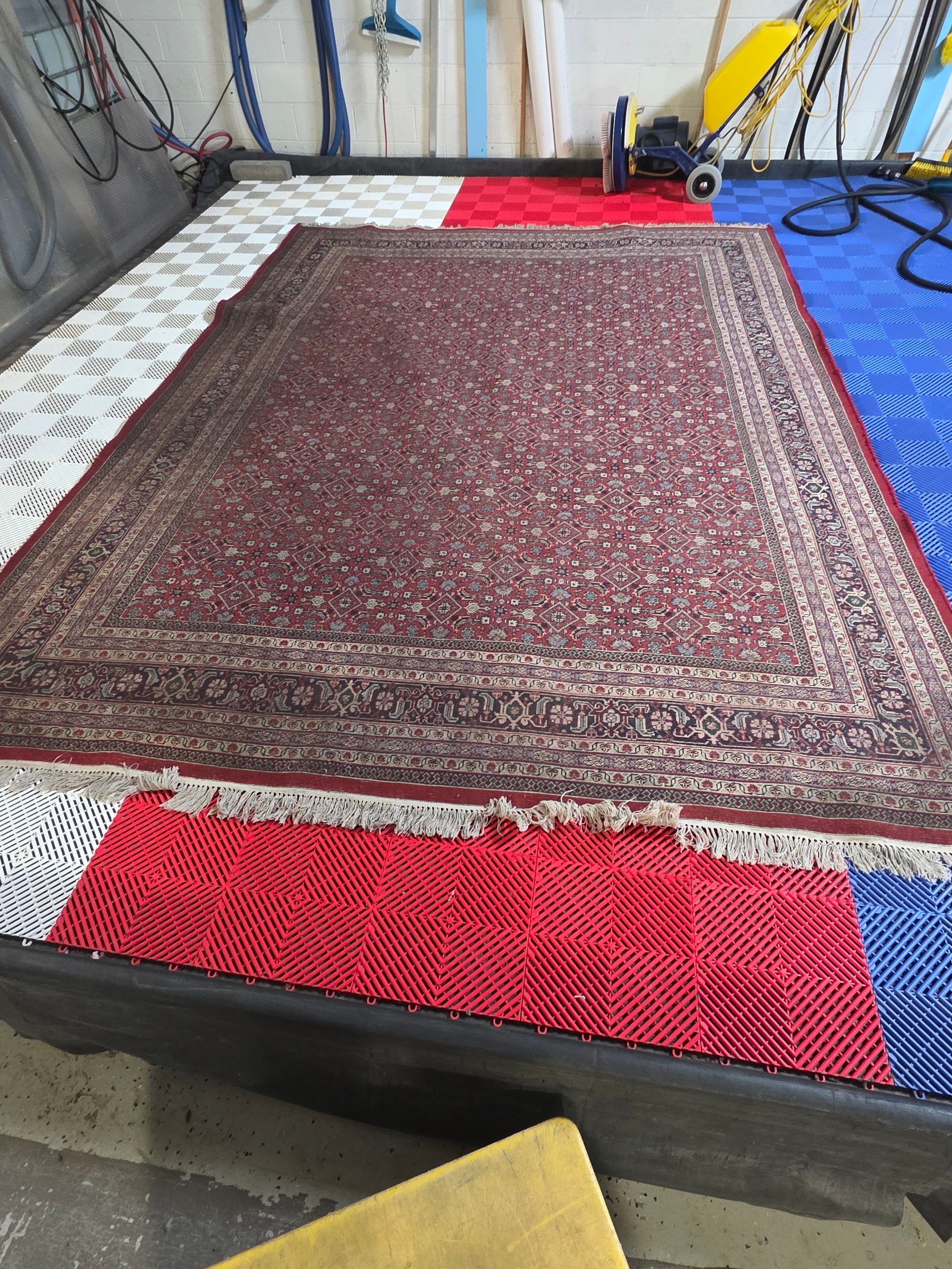 Large patterned rug laid on a raised platform, with red, white, and blue floor mats around it.
