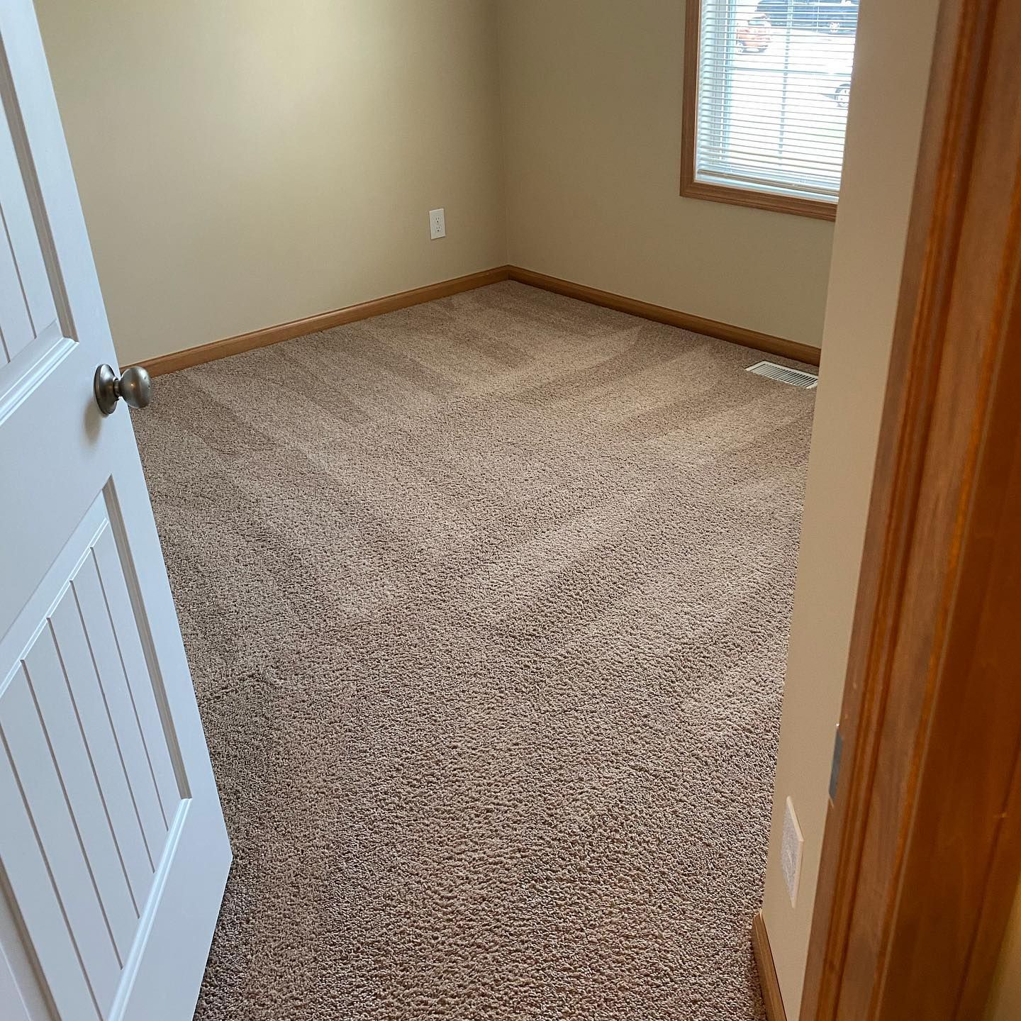 An empty room with beige walls and textured brown carpeting, viewed through an open white door.