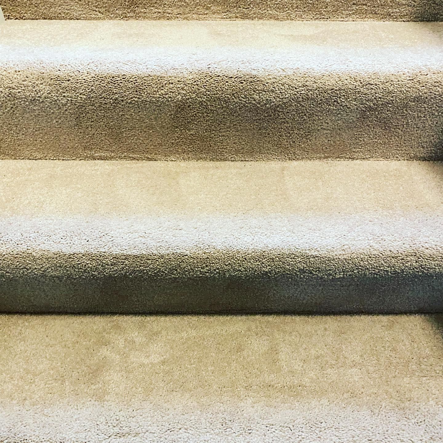 A close-up view of three parallel, beige concrete steps with a textured surface.