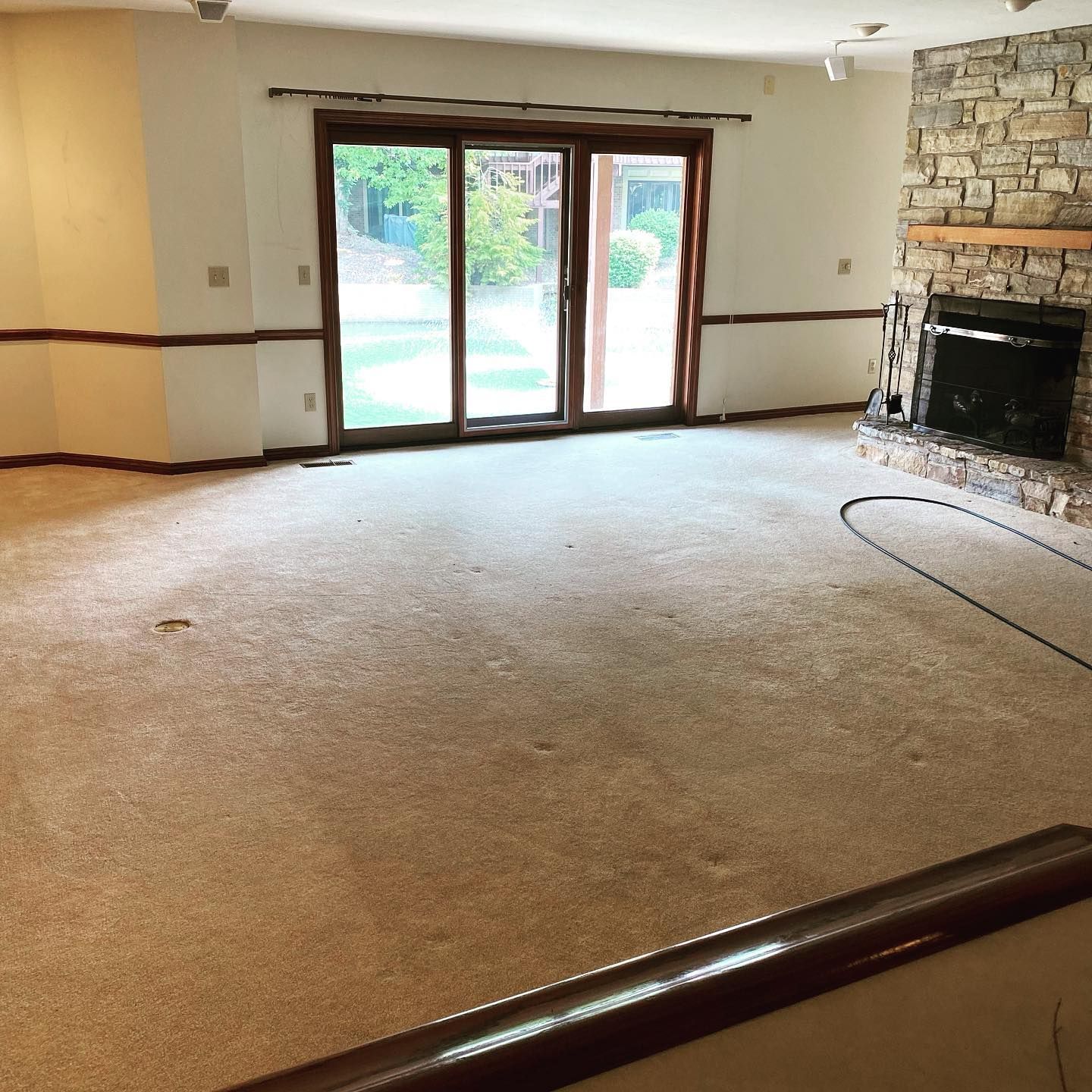 A living room with beige carpeting, a stone fireplace, and large sliding glass doors leading to a patio.