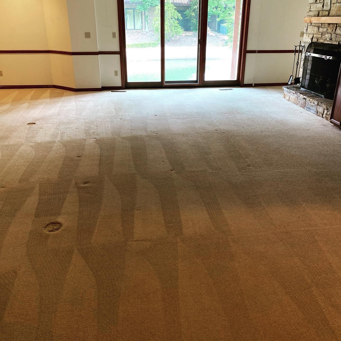 A living room with freshly vacuumed tan carpet, a stone fireplace on the right, and large sliding glass doors in the back.