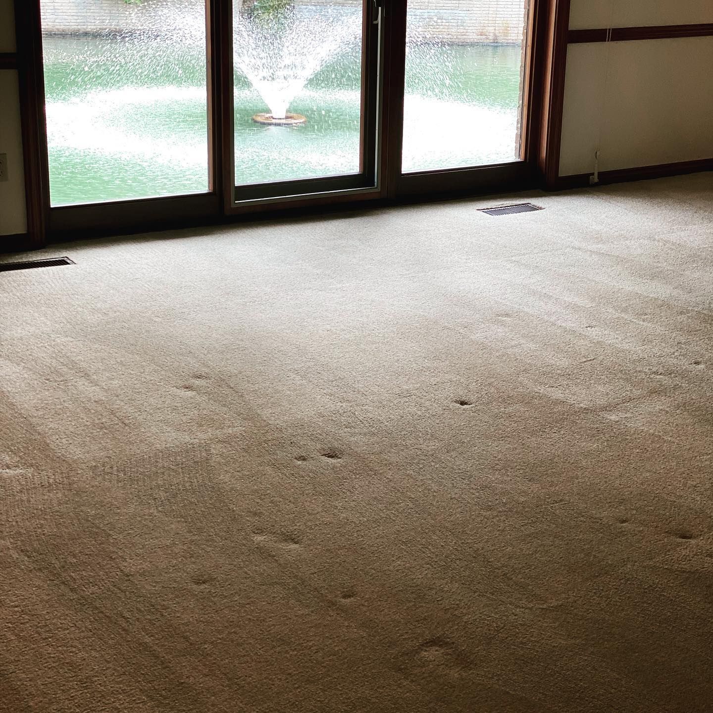 A carpeted room looks out through glass sliding doors at a fountain in a pond.