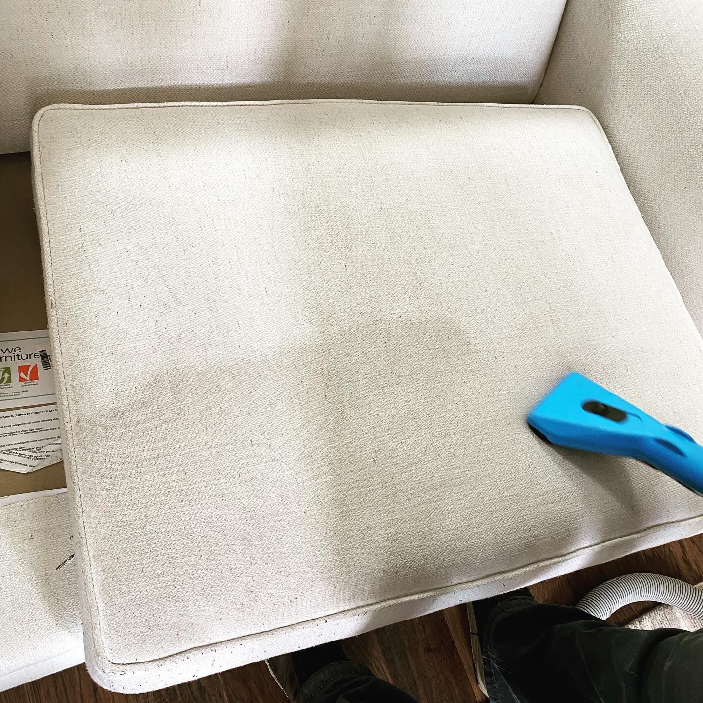 A blue upholstery cleaning tool cleans a section of a beige fabric chair cushion.