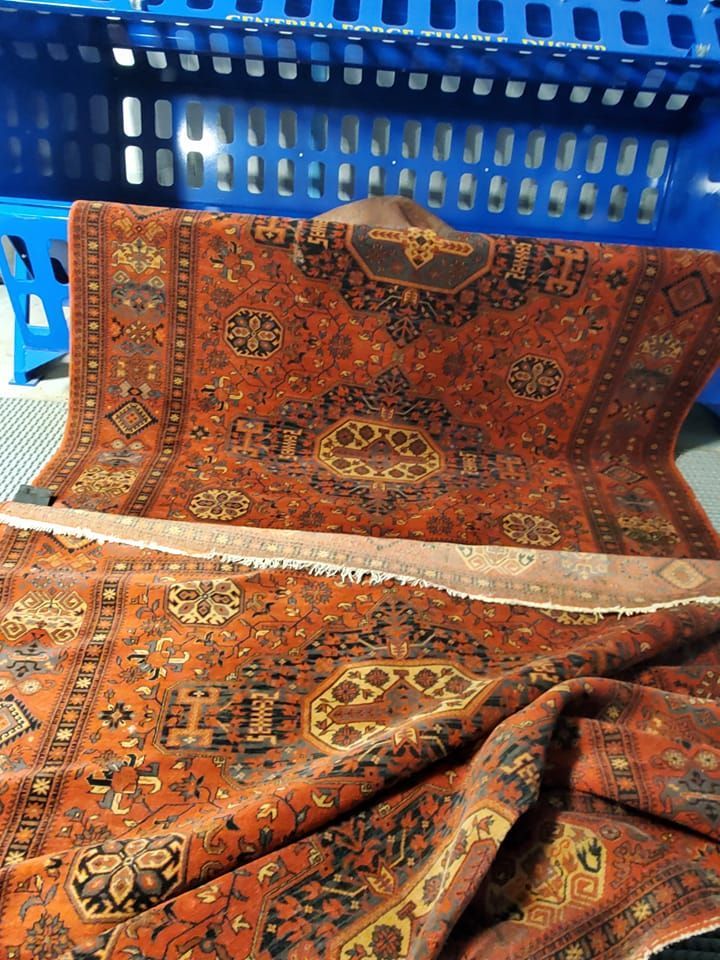 A folded, rust-colored Persian-style rug with intricate floral and geometric patterns resting in front of blue crates.