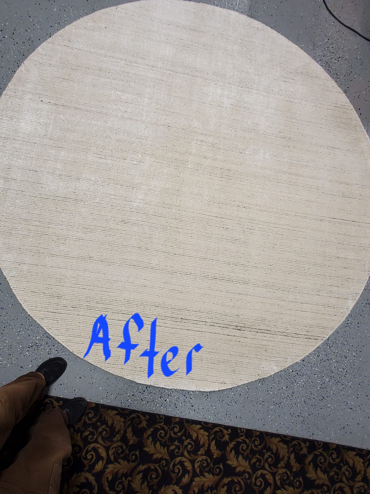 A circular, light-colored rug lies on a speckled gray floor, with the word 