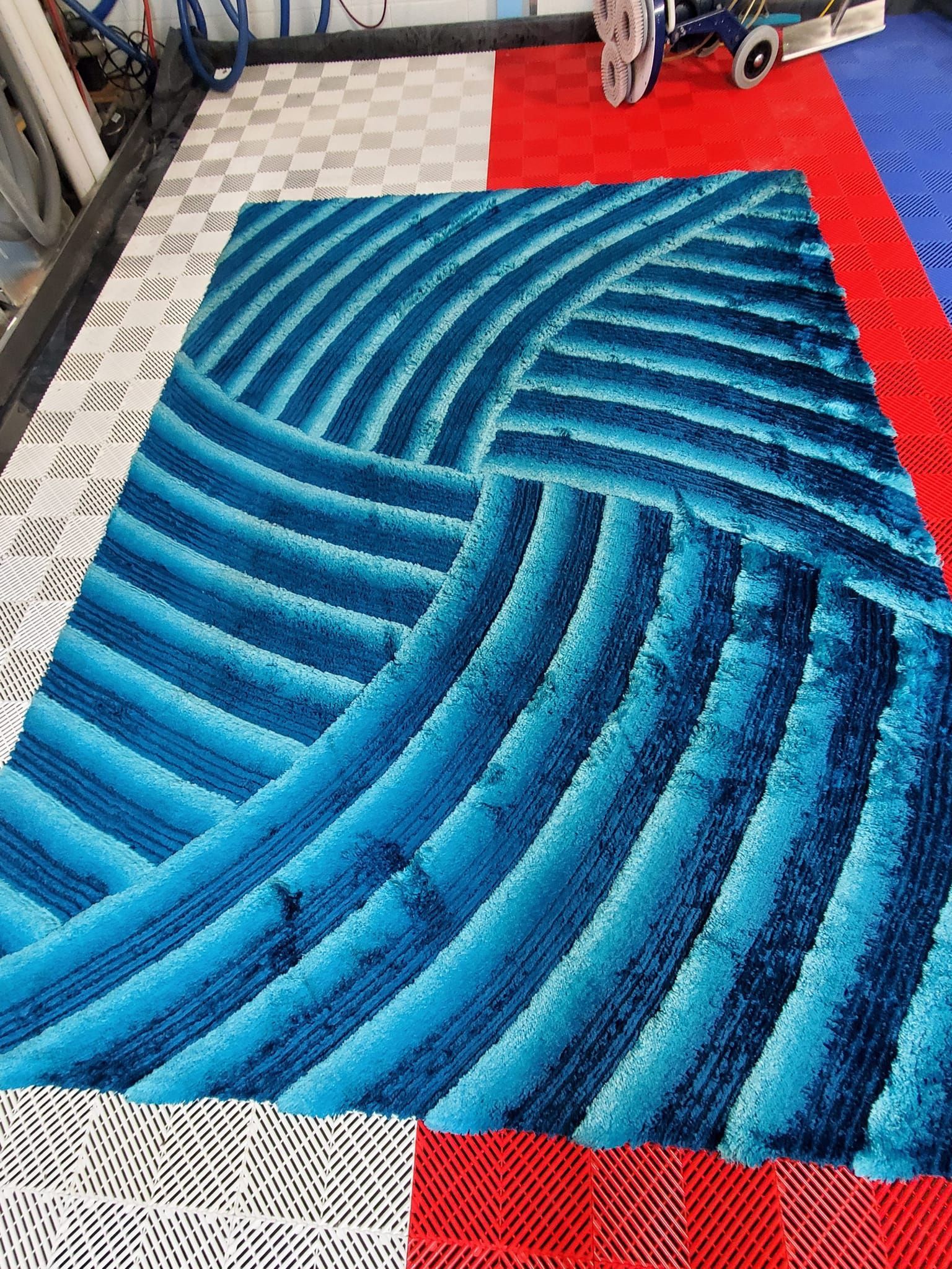 A bright blue shag rug with a textured, curved striped pattern, placed on a floor with red and white patterned sections.