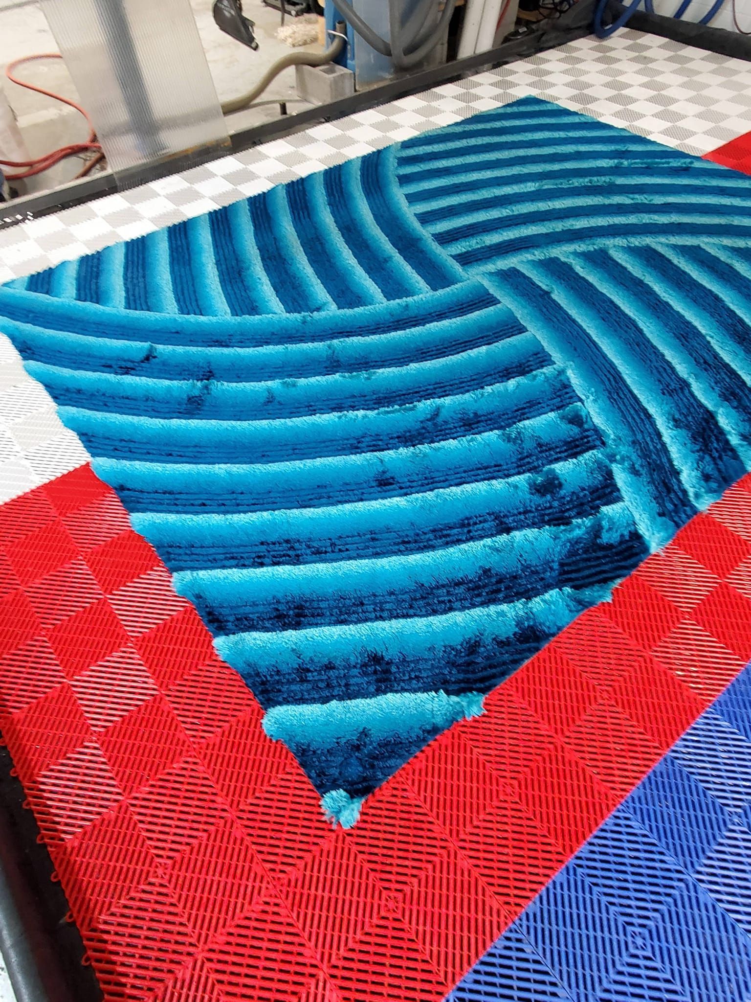 A shaggy blue rug with a striped pattern sits on a tiled floor with red and blue interlocking plastic tiles.