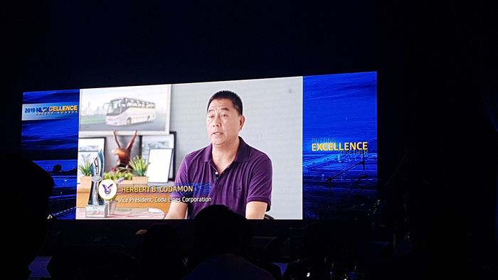 A man is talking on a large screen in a dark room.