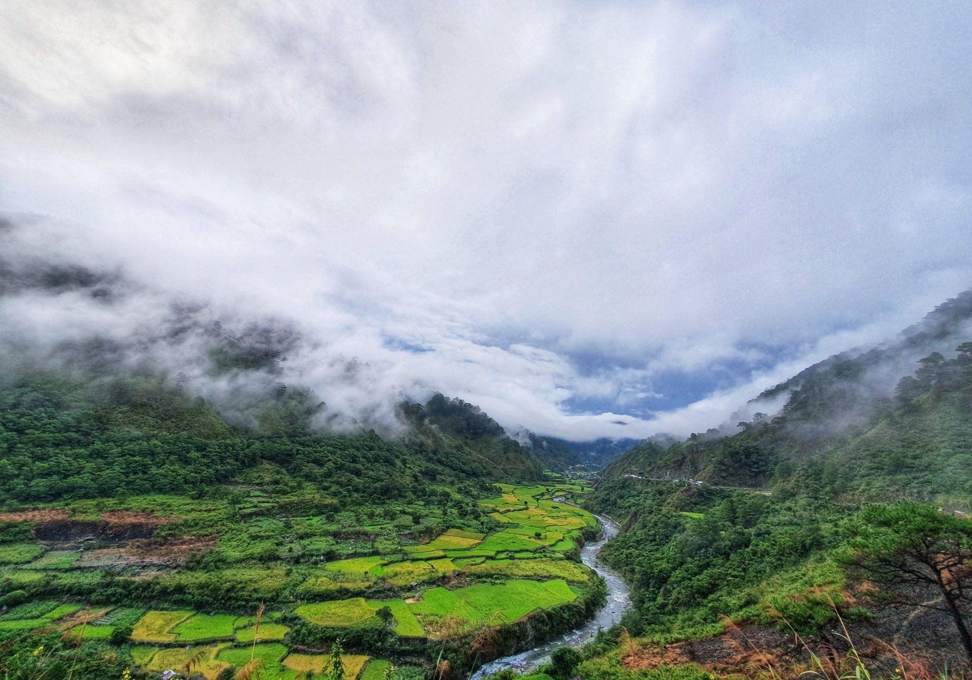 A river flowing through a lush green valley surrounded by mountains and clouds.