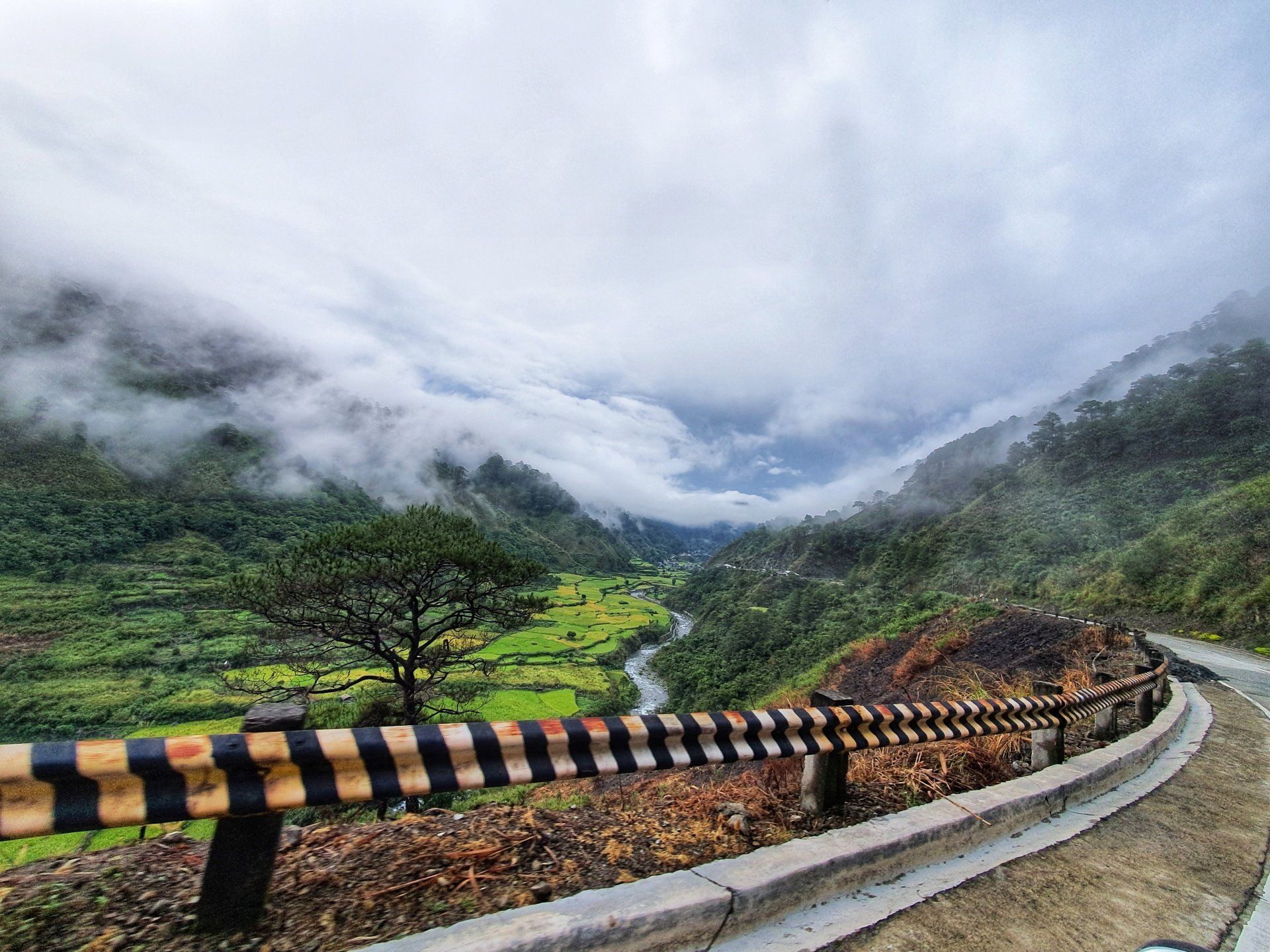 A road with a fence on the side of it going through a mountain valley.