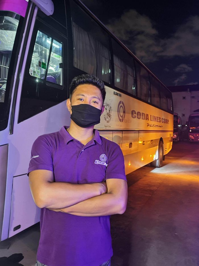A man wearing a mask is standing in front of a bus