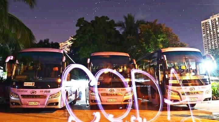 A group of buses are parked in a parking lot at night.