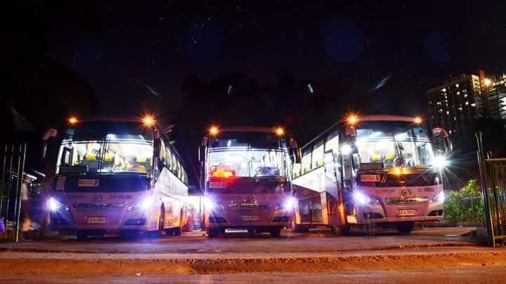 Three buses are parked next to each other on the side of the road at night.