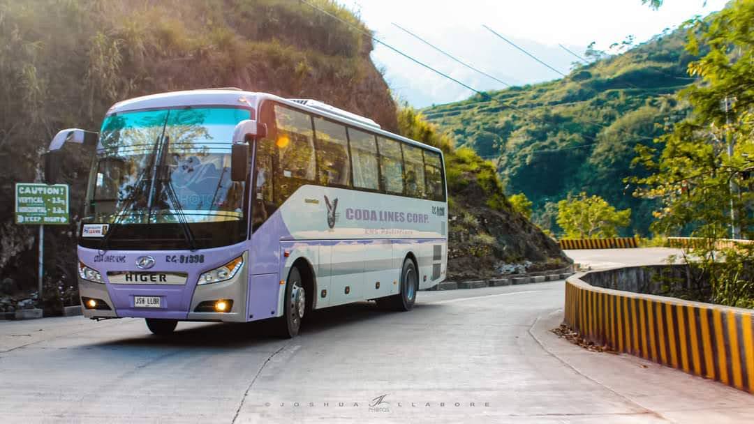 A purple and white bus is driving down a curvy road.