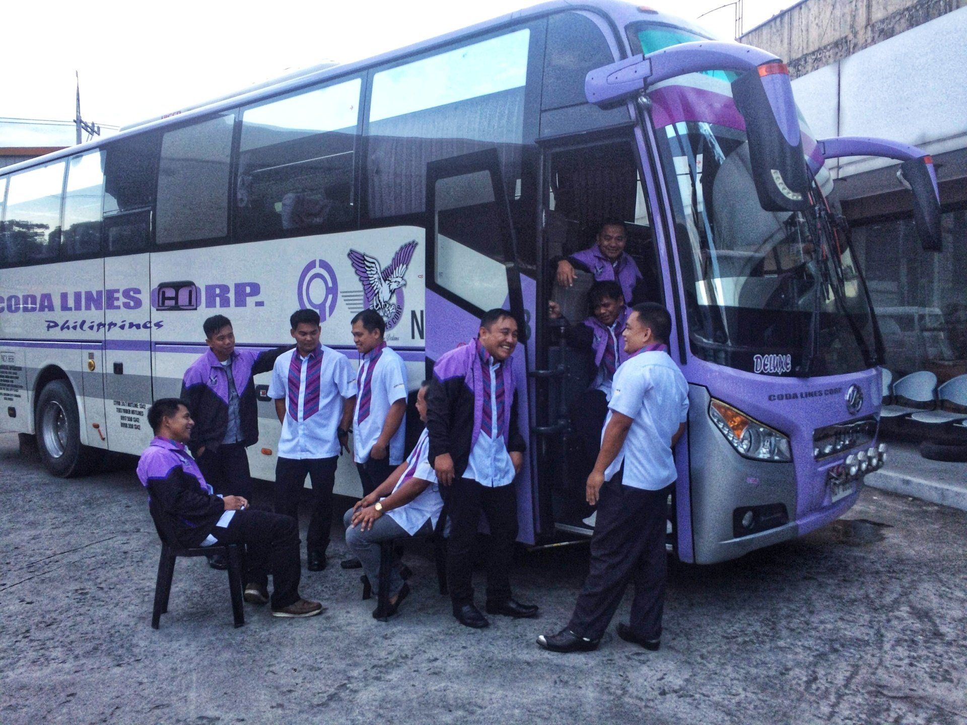 A group of people are standing in front of a purple bus.