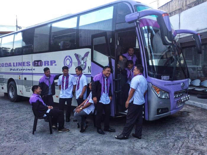 A group of people are standing in front of a purple bus.