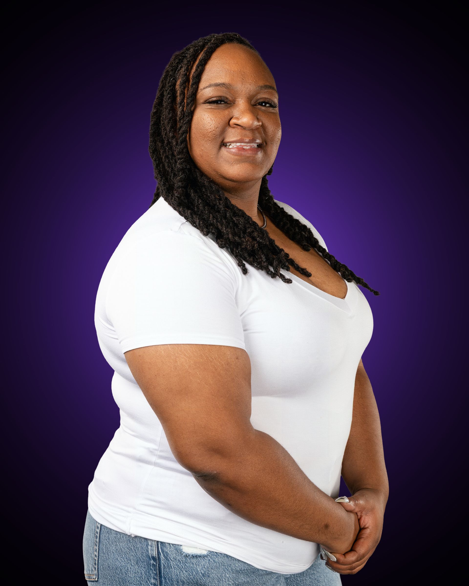Woman with blonde hair wearing a purple long-sleeved shirt, smiling with arms crossed in front of a gray background.