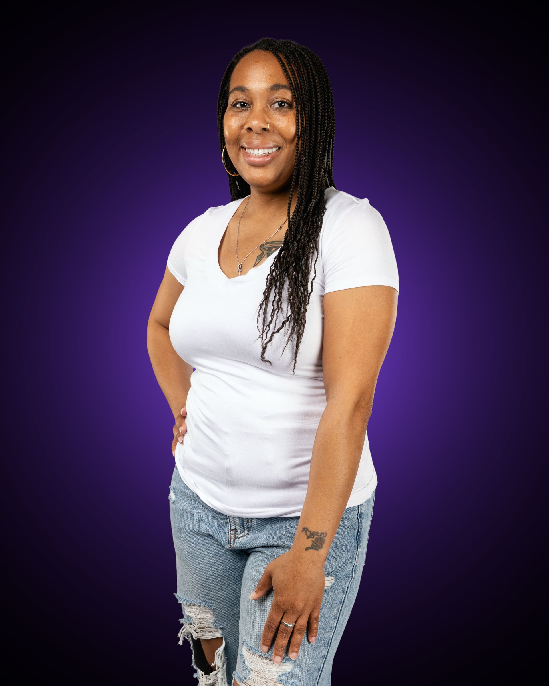 Woman with curly brown hair and a blue shirt smiles with arms crossed.