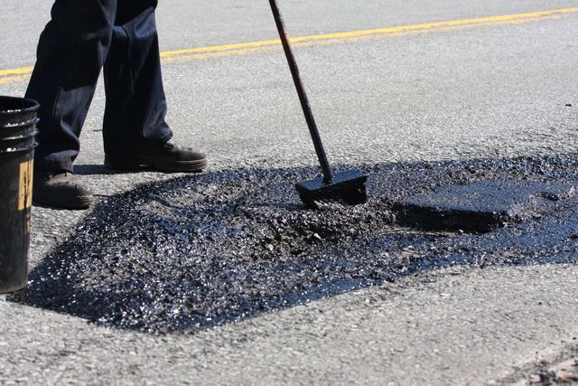 Worker spreading fresh asphalt over a road pothole with a shovel