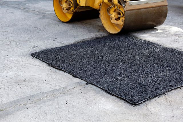 Road roller compacting fresh black asphalt patch on a concrete surface