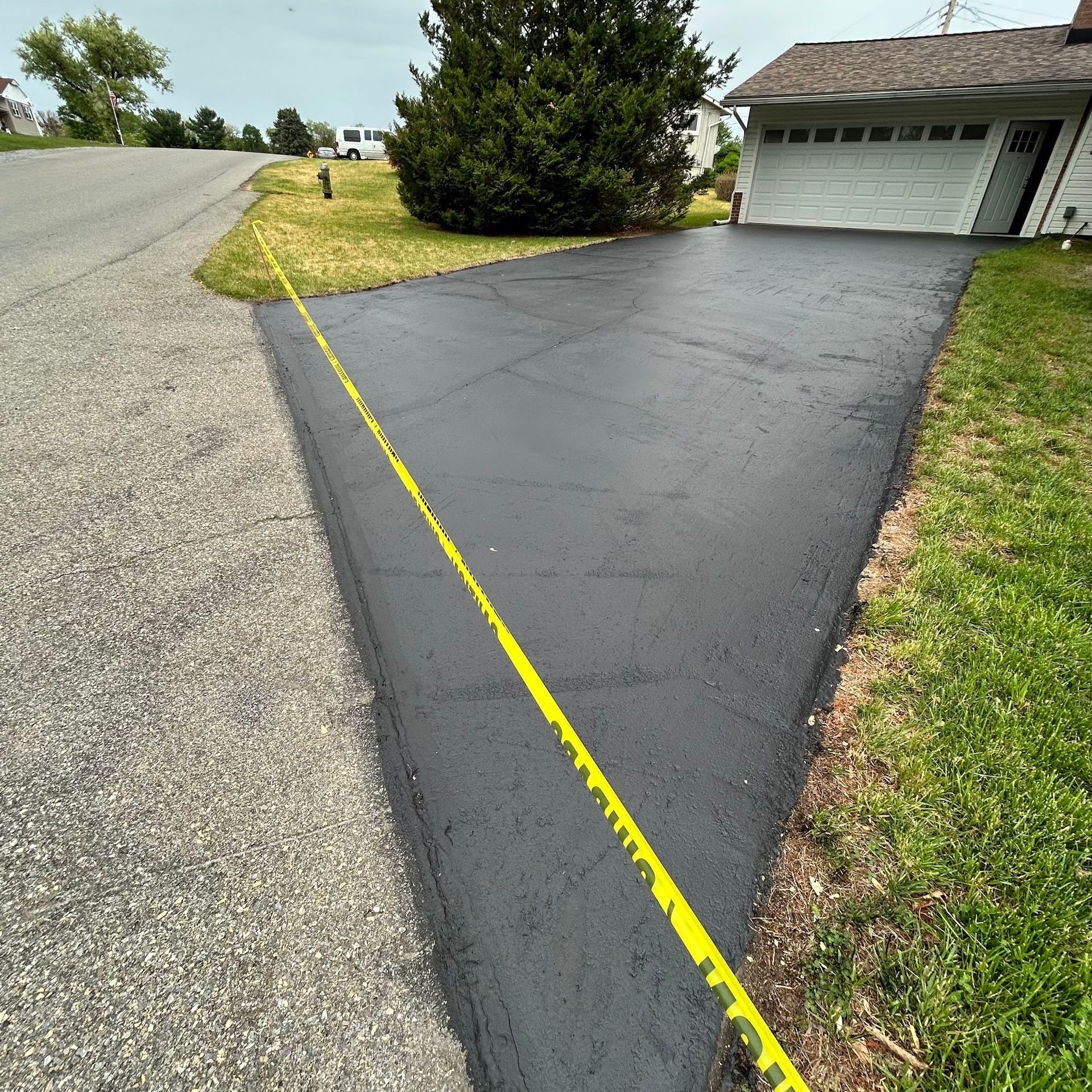 Freshly paved black driveway beside a garage, marked with a yellow line along the edge.