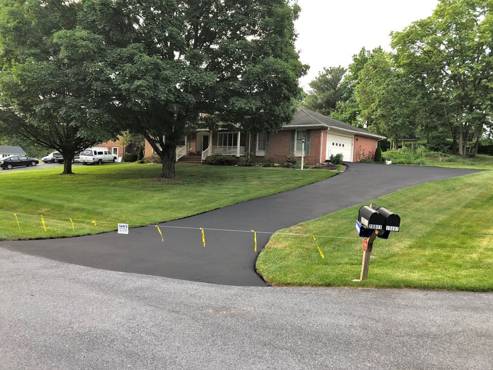 Suburban house with a long paved driveway, green lawn, and black mailbox beside the road